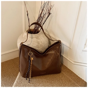 Détail du sac en cuir marron avec pendentif étoile, pompon et logo doré imprimé