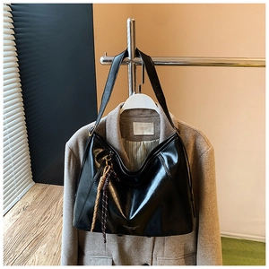 Détail du sac cabas en similicuir noir avec pompon tressé élégant et logo doré