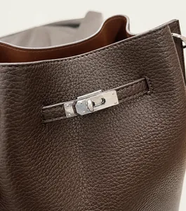 Detail of lychee pattern leather bucket bag with silver hardware lock and strap