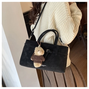 Lifestyle foto van een zwarte suède handtas met teddybeer hanger op een gebreide trui