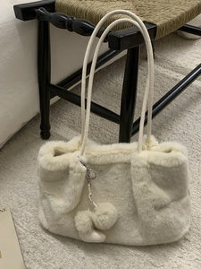 Grand sac fourre-tout beige en fausse fourrure avec pompons sur une chaise pour l'hiver