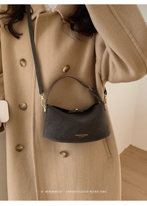Detail of dark grey suede bucket bag with gold logo shown on model with beige coat