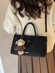 Minimalistische zwarte lederen handtas met beerhanger, gestyled met beige breigoed