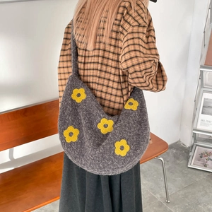 Détail d'un sac cabas en tricot gris avec des motifs de fleurs jaunes sur l'épaule