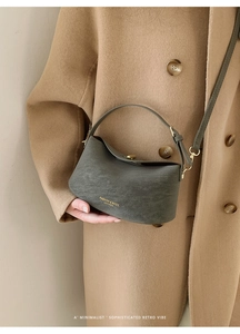 Close-up of a sage green minimalist leather bucket bag with a gold embossed logo and strap