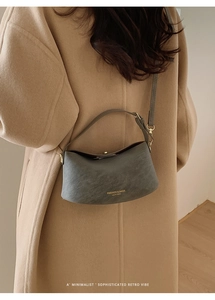 Detail of dark grey crescent shoulder bag featuring gold fashion logo and textured leather
