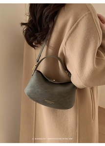 Detail view of dark grey matte leather bucket bag with gold lettering on a wool coat