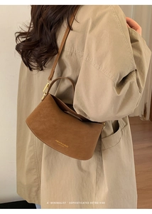 Detail of a brown suede half-moon crossbody bag with golden lettering on a beige coat