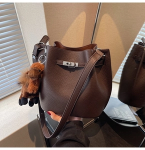Detail of dark brown lychee leather bucket bag with silver turn-lock and camel charm