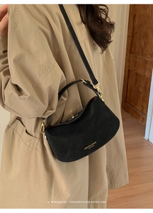 Close-up of black matte leather shoulder bag with gold hardware worn by model