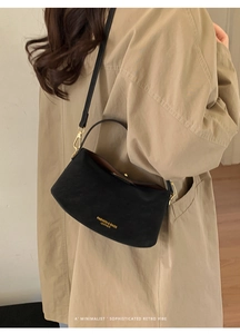 Detail of black leather crossbody bucket bag with gold hardware and logo on trench coat