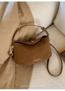 Close-up of brown suede leather bucket bag with gold lettering and minimalist shoulder strap