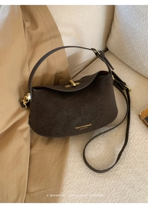 Detail of dark brown leather bucket bag with gold clasp and fashion logo on beige sofa
