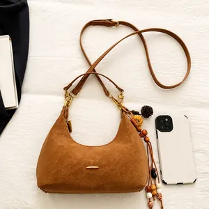Detail shot of brown crescent bag featuring matte suede texture and ethnic tassel charm