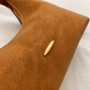 Detailed close-up of brown faux leather texture and gold-tone FNDF metal logo on handbag