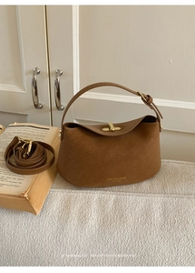 Close-up of brown leather handbag with gold metal lock and elegant fashion text detail