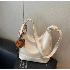 Detail view of cream leather tote bag with bear charm and golden metal hardware