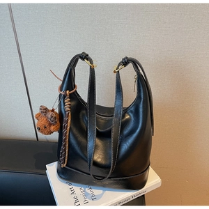 Detail of black leather bucket bag with white contrast stitching and a small bear charm