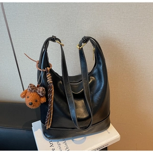 Detail of black leather hobo bag featuring white contrast stitching and a plush bear charm