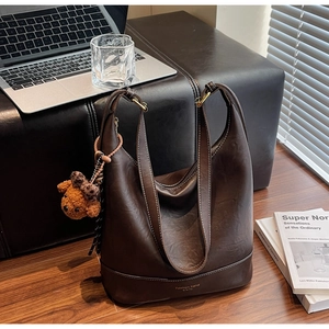 Detail of deep brown leather hobo tote with a cute teddy bear charm on wooden floor