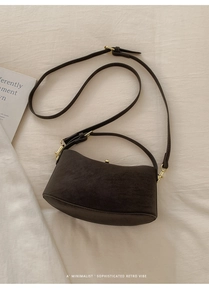 Detailed shot of dark brown suede half-moon bag with gold metal buckle on white fabric