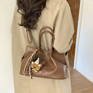 Sac à main en cuir marron avec charm ours porté sur un trench-coat kaki élégant