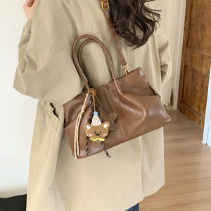 Sac fourre-tout marron vintage avec charm ours porté sur un trench-coat de couleur kaki