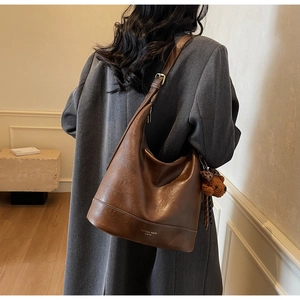 Close-up of brown textured leather tote with adjustable strap and bear charm accessory