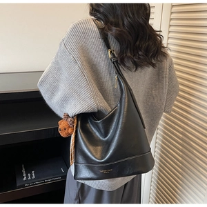 Detail view of black leather hobo tote bag with plush bear charm and fashion text