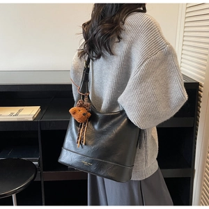 Detail of black leather hobo bag with cute brown plush bear charm and fashion text branding