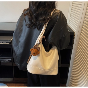 Detail of a creamy leather tote bag with a brown teddy bear charm and logo print