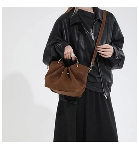 Détail d'un sac seau en daim marron avec poignées anneaux dorés et bandoulière en cuir souple