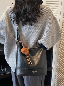 Large black shiny leather tote bag with a teddy bear charm shown on a casual model