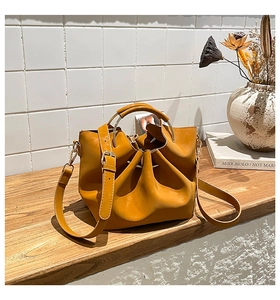Détail du sac seau plissé jaune gingembre avec poignée en anneau métallique sur bois