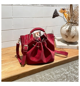 Détail d'un sac seau rouge en cuir mat avec une large poignée et fermeture à cordon