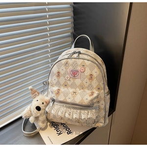 Détail du sac à dos crème avec imprimés ours, étiquette cerise rose et bordure en dentelle