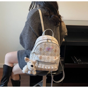 Détail du sac à dos matelassé crème avec bordure en dentelle et porte-clé peluche