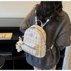 Vue détaillée du sac à dos matelassé beige avec volants en dentelle et pendentif chien