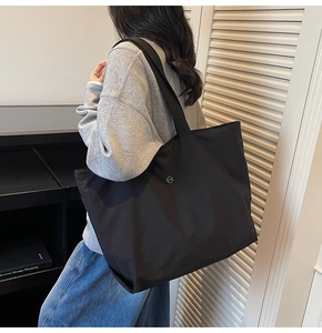 Detalle de un bolso tote negro grande que muestra el logo metálico y la textura de nailon