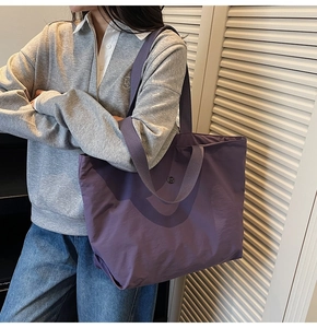Detalle del bolso tote morado oscuro de gran capacidad con correa larga y logo de metal