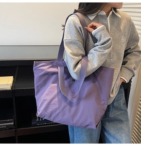 Detalle de un bolso tote grande de tela morada con cierre magnético y asa de hombro