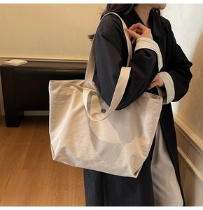Detalle de bolso tote grande de tela beige mostrando la correa de hombro y botón metálico