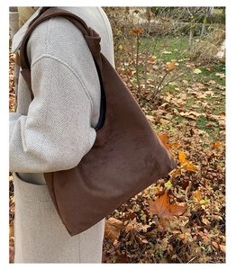 Detail of dark brown suede hobo bag with knotted shoulder strap in outdoor autumn setting