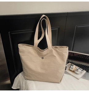 Primer plano del bolso tote beige de gran capacidad con logo metálico en estilo urbano