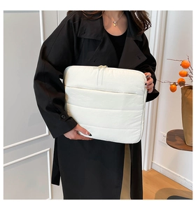 White quilted laptop sleeve with dual zippers held by a person in a black coat