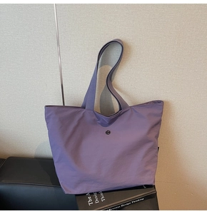 Detalle de un bolso tote de tela morado con textura de nailon y logo metálico redondo