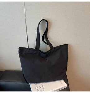 Detalle de bolso tote negro minimalista de tela con broche de metal y correas de lona gruesa