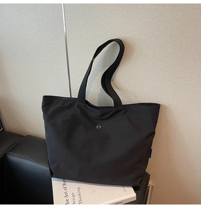 Primer plano de un gran bolso tote negro en un sofá con correa ancha para el hombro