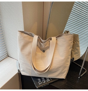 Primer plano de un bolso tote beige con asas tejidas anchas y cierre magnético de metal