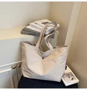Detalle del bolso tote grande de tela beige con textura arrugada y cierre de botón redondo